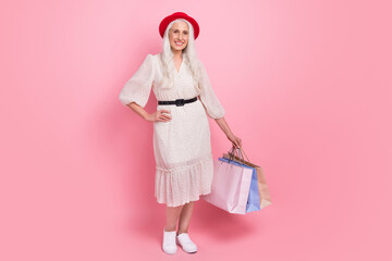 Full length body size view of attractive cheerful grey-haired woman posing carrying new things isolated over pink pastel color background