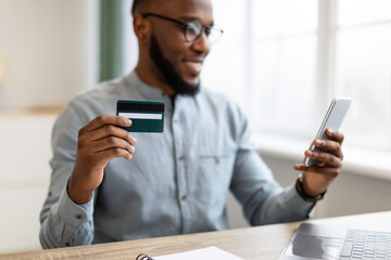 Obraz na płótnie Canvas Black Businessman Using Credit Card And Smartphone Sitting In Office