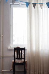 Lonely little girl at home sits by the window with her back to the camera. autism awareness day/ Autism concept