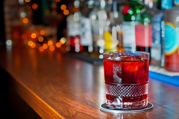 Yellow cocktail on bar counter. Whiskey, rum or brandy on the background of bottles with alcohol. Glass with booze on a wooden board.