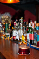 Yellow cocktail on bar counter. Whiskey, rum or brandy on the background of bottles with alcohol. Glass with booze on a wooden board.