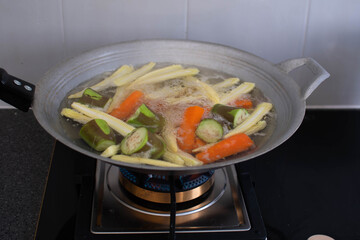 Eggplant, carrots, baby corn were turned into pieces. And boil it in a pan Many kinds of mixed vegetables are cooked in an iron pan. The iron pan is boiling vegetables on the kitchen gas stove.