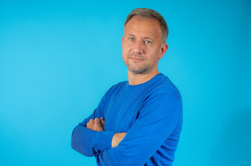 Handsome young man smiling with arms crossed over blue background