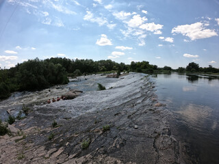 Water flows through the dam of Mygiivska HPP. Rapids and river dam on the Southern Bug. Group of people resting on the river water.