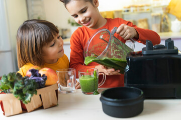 Children pour and eating green smoothies from blender in the kitchen. Funny Brother and Sister Make Healthy Breakfast together. Cute kids learn Healthy Habits and how to make green cocktail