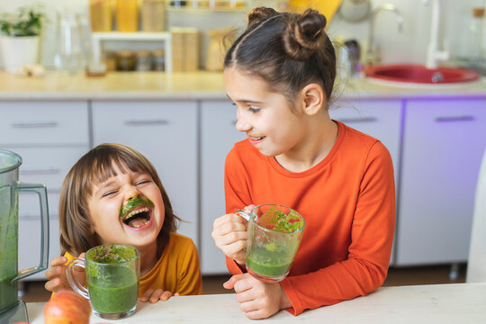Happy Kids with glass cup of green smoothies in hands. Cute boy and girl crazy drinks healthy dietary nutritious cocktail at home in the kitchen. Healthy lifestyle, raw food
