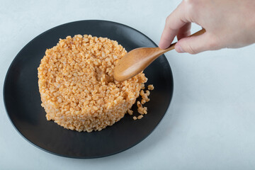 Woman hand taking spoon of bulgur pilaf from dark plate