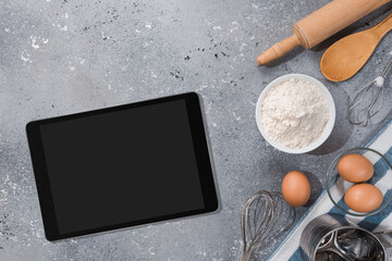 Ingredients, tools for baking and tablet with blank screen and place for text or image on gray table. recipe, cookbook, cooking courses online template