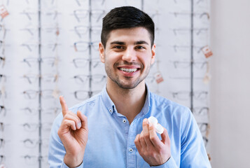 Happy guy holding contact eye lenses in optics shop