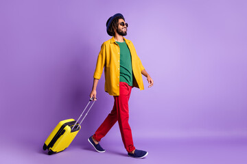 Full size profile portrait of positive dark skin guy carry suitcase look empty space isolated on purple color background