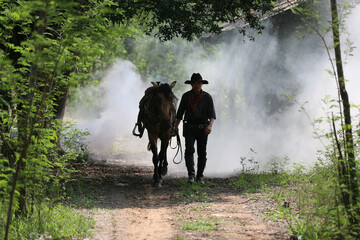 The silhouette of  rider as cowboy outfit costume with a horses and a gun held in the hand against...