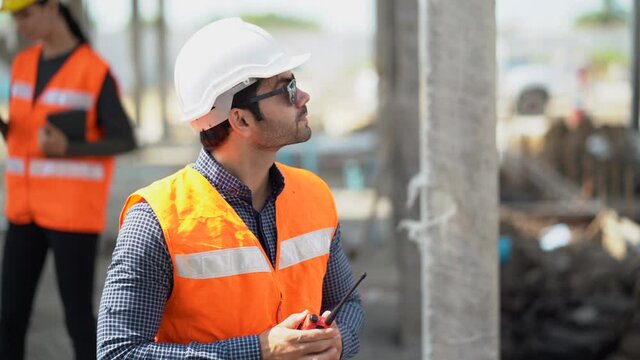 builder in hard hat  talking by walkie talkie control and communication with worker outdoors on construction site at village . contractor using radio operation in industry