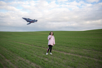 A girl flies a kite on a large green field. Blue cloudy sky at background. .
