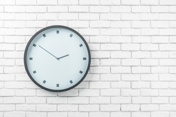White round wall clock in black frame on the left side of light brick wall