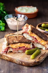 Toasted Reuben sandwich on a wooden board served with Russian dressing, sauerkraut and dill pickles.