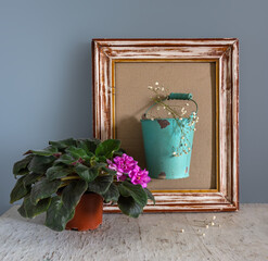 Still life with blooming violets and a bucket of white flowers in a wooden frame. Vintage.
