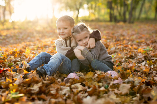Cute children, boy and girl are playing, sitting and hugging together in autumn park.
