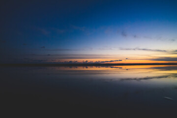 波の水たまりに反射した夕日と空と雲