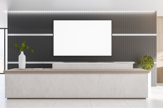 Blank white poster on dark wall above marble reception desk in modern sunny office hall. Mockup