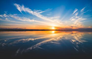 Fototapeta na wymiar 波の水たまりに反射した夕日と空と雲