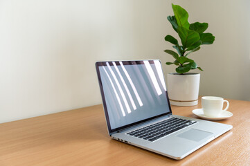 White screen Laptop computer with monstera plant, coffee cup and smart phone on wooden table, copy space