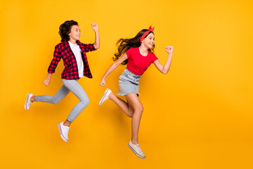 Full length profile portrait of two little energetic crazy pupils enjoy running isolated on yellow color background