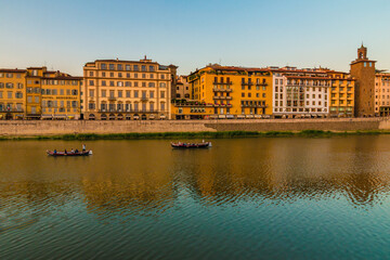 Fototapeta na wymiar Lovely Arno riverbank view along Lungarno degli Acciaiuoli street in Florence's historic city centre at dusk. Two vintage Florentine Gondola boats, so called Barchetto, are having a romantic cruise.