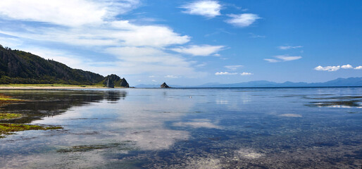 White clouds reflect on the mirror-like surface of the water. In the early morning the sea is completely.  calm .Kunasir island. Low tide