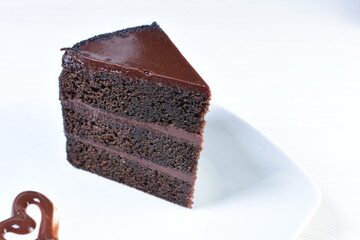 Decorated chocolate cake on white plate and light colored wooden background