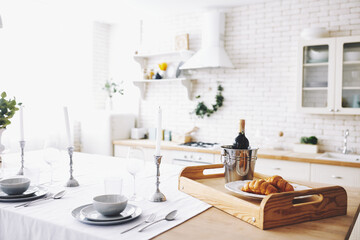 Table set for an event, party, date or wedding with white candle and bottle of wine with croissant. Grey dishes on white kitchen. Beautiful breakfast 