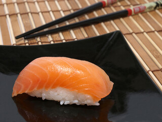 Smoked salmon sushi on black plate on a bamboo mat close-up