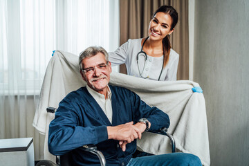 Portrait of two happy people, a nurse and an old grandfather in a wheelchair. The nurse takes care of him in a blanket. Nursing home