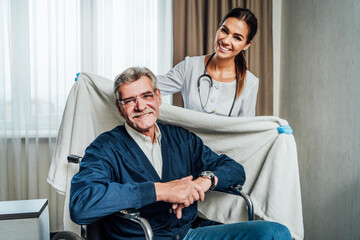 Obraz premium Portrait of two happy people, a nurse and an old grandfather in a wheelchair. The nurse takes care of him in a blanket. Nursing home