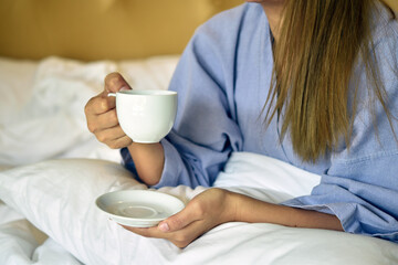 Woman sitting in bedroom drinking coffee in the morning.
