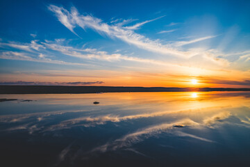 波の水たまりに反射した夕日と空と雲