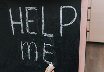 Little girl, child writes words and asks all people for help on a wooden black board, easel,...
