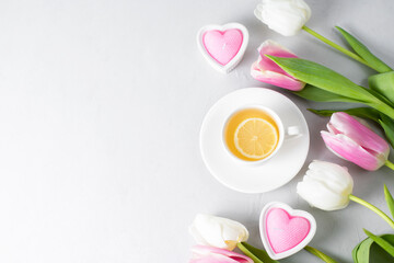Fototapeta na wymiar Tulips with white cup of tea on a light background. Spring tenderness still life composition with candles. Flowers for romantic, love atmosphere. Relax, meditation pause. Selective focus, copy space.
