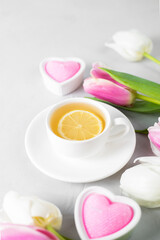 Tulips with white cup of tea on a light background. Spring tenderness still life composition with candles. Flowers for romantic, love atmosphere. Relax, meditation pause. Selective focus, copy space.