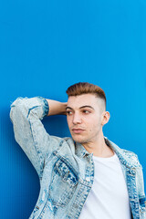 Portrait of an isolated young man looking confident and wearing a denim jacket in a blue background