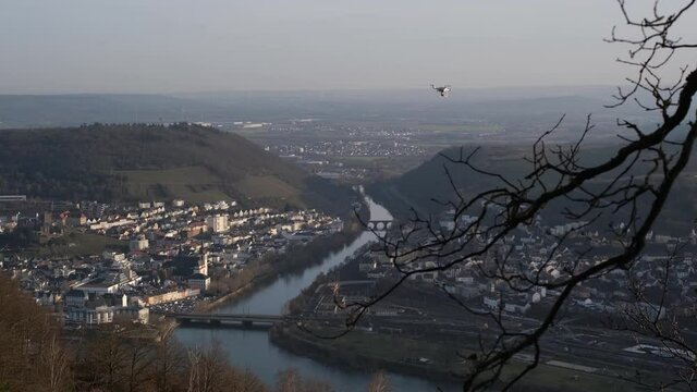 Hovering multicopter taking pictures of winter nature. Small white drone with rotating propellers flying near the Rhine River at R&uuml;desheim am Rhein. Flying drone outdoors, afternoon, sunset lights, 4k