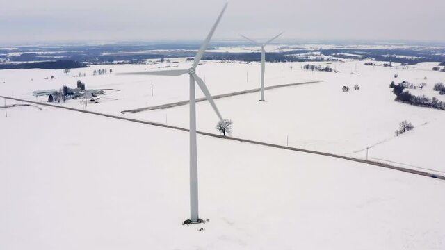 Aerial view of two wind turbine towers on countryside land covered by snow, winter scenery