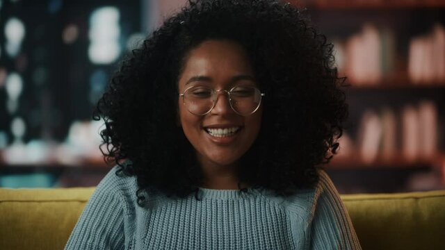 Close Up Portrait of a Happy Laughing Young Latina with Afro Hair and Glasses Posing for Camera at Home. Beautiful Diverse Multiethnic Hispanic Female Wearing Blue Jumper in Living Room.