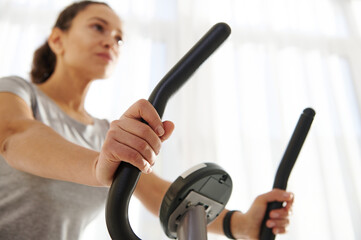Closeup of hands of woman riding a stationary bicycle during a cardio workout at home