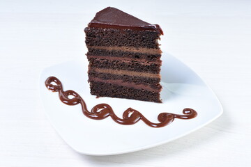 Decorated chocolate cake on white plate and light colored wooden background