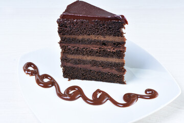 Decorated chocolate cake on white plate and light colored wooden background