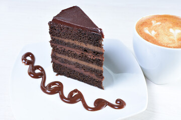 Decorated chocolate cake on white plate and light colored wooden background