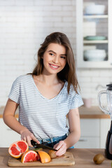 cheerful woman looking away while cutting fresh fruits in kitchen