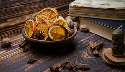 Fototapeta na wymiar plate with dried orange slices on the table and natural wax candle on a dark wooden table. selective focus.