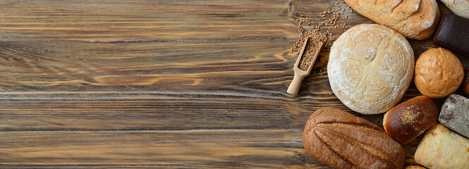 Different types fresh bread on wooden background with space for text