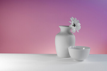 chrysanthemum flower in a white vase and white cup beside on a white table top and pink background, minimalist still life with copyspace